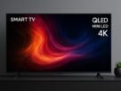 Smart TV TCL de 75 polegadas QLED Mini LED 4K em uma sala moderna, exibindo cores vibrantes em tons de vermelho e azul, sobre um móvel escuro com vaso decorativo ao lado e parede cinza ao fundo.