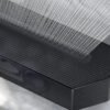 Close de uma soundbar preta mostrando a grade frontal e o interior dos alto-falantes, com representação visual das ondas de som saindo do aparelho.