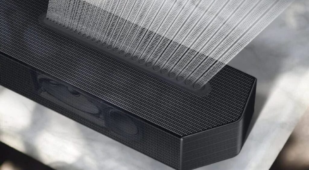 Close de uma soundbar preta mostrando a grade frontal e o interior dos alto-falantes, com representação visual das ondas de som saindo do aparelho.